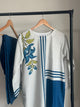 White shirt with blue floral embroidery on a hanger against a neutral background